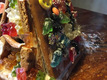 Ein bunt dekoriertes Lebkuchenhaus, überzogen mit verschiedenen Gummibärchen, Süßigkeiten und bunter Glasur. Die Süßigkeiten sind vielfältig angeordnet und verleihen dem Haus ein fröhliches, festliches Aussehen. Der Hintergrund ist aus Holz, was dem Bild eine gemütliche Stimmung verleiht.