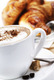 Das Bild zeigt eine Tasse Cappuccino und im Hintergrund Croissants