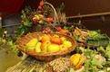 Ein Tisch mit mehreren Obst- und Gemüsekörben, darunter Äpfel, Birnen und frittierte Kürbisse. Dekoration aus frischen Kräutern und Trockenblumen umrahmt die Arrangements. Die Vielfalt der Farben und Texturen vermittelt eine herbstliche Atmosphäre.