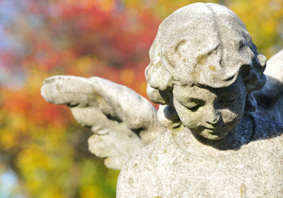 Engelfigur aus Beton auf einem Friedhof. Buntes Laub, verschwommen, im Hintergrund