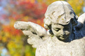 Engelfigur aus Beton auf einem Friedhof. Buntes Laub, verschwommen, im Hintergrund