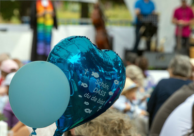 Zwei Luftballons beim "Main Tauffest 2022". Einer ist herzförmig und trägt die Aufschrift "Schön, dass du da bist".
