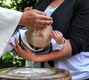 Das Foto zeigt ein kleines Kind auf dem Arm seiner Mutter, das gerade getauft wird.