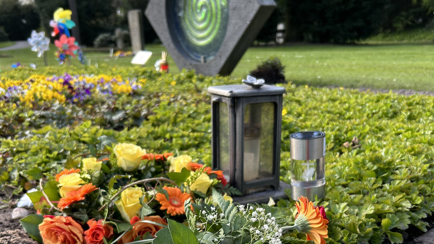 Eine Grabstelle mit Blumen und bunten Windrädern.