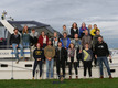 Eine große Gruppe Menschen steht auf und vor einem Boot verteilt für ein Gruppenbild der gesamten Mannschaft.