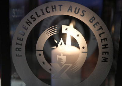 Eine Kerze erleuchet das Logo der Firiedenslichtaktion auf einer Glasscheibe.
