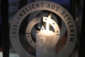 Eine Kerze erleuchet das Logo der Firiedenslichtaktion auf einer Glasscheibe.