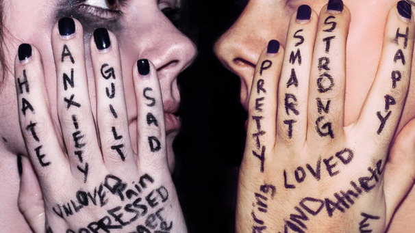 Das Foto zeigt zwei weibliche Gesichter, die ihre Wangen mit ihren tätowierten Händen umfassen. Zu lesen sind Worte wie Krieg, Hass, Liebe oder Depression. Das künstlerische Foto soll Empfindungen angesichts von Gewalterfahrungen zum Ausdruck bringen.