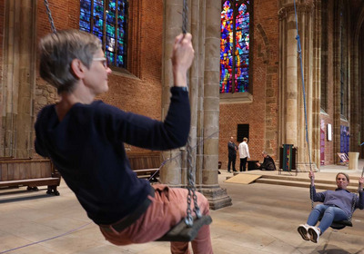 Das Foto zeigt eine Kunst-Installation in der Bremer Stadtkirche Unser Lieben Frauen. Zwei Frauen schaukeln miteinander im Takt.