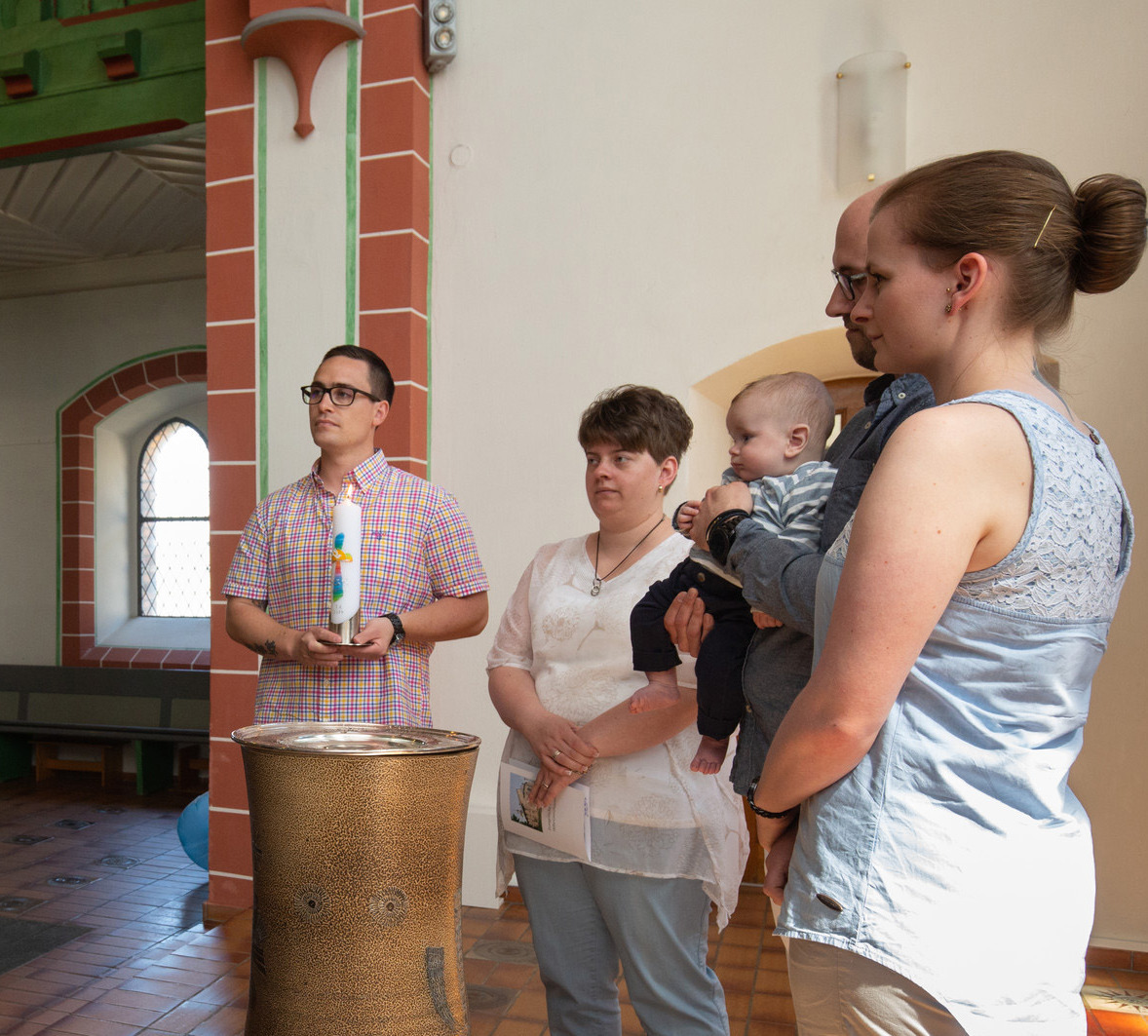 Foto von einer Familie mit Baby am Taufstein. Eine Pastorin segnet sie.
