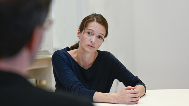 Das Symbolphoto zeigt eine Beratungssituation. Im Vordergrund ein Klient von Hinten. Ihm gegenüber eine Frau, die ihm zuhört