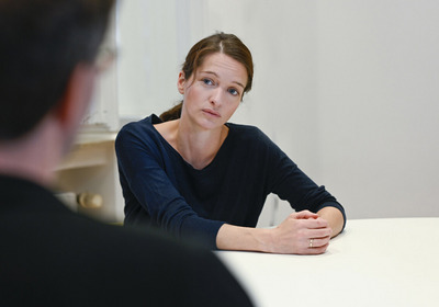 Das Symbolphoto zeigt eine Beratungssituation. Im Vordergrund ein Klient von Hinten. Ihm gegenüber eine Frau, die ihm zuhört