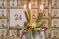 Das Foto zeigt vier goldene Kerzen vor einem Adventskalender