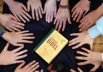 Hände der Konfirmanden um eine Bibel herum