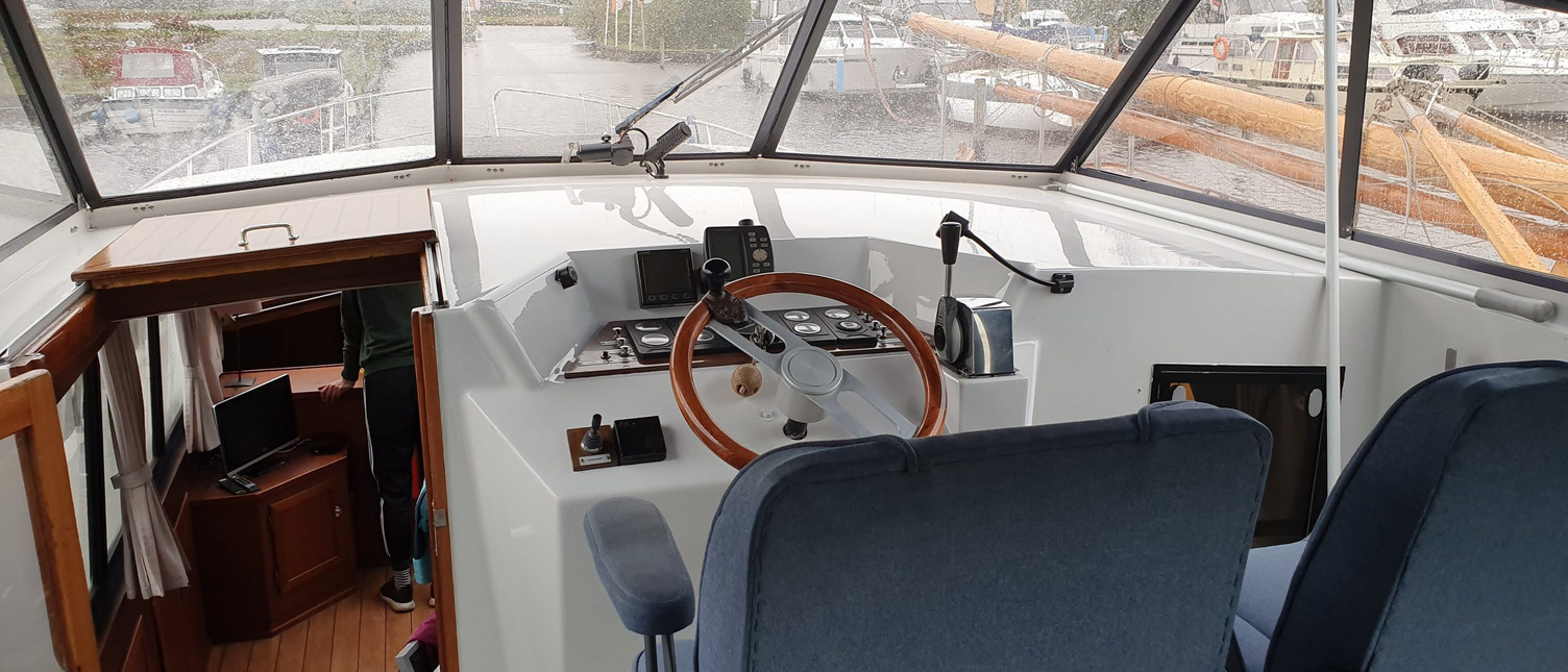 Der Innenraum der Persenning auf einem Boot. Zwei Sitzen stehen vor dem Steuerstand. Links davon ist eine Tür und eine Treppe die hinunter in das Innere des Bootes führen. 