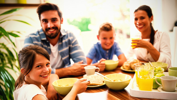 Das Foto zeigt eine fröhliche Familie beim gemeinsamen Frühstück