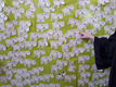 Eine bunte Wand mit vielen handgezeichneten Schafen, jedes mit einem Namen beschriftet. Eine Hand zeigt auf eines der Schafe. Der Hintergrund ist grün und die Schafe sind schwarz-weiß.