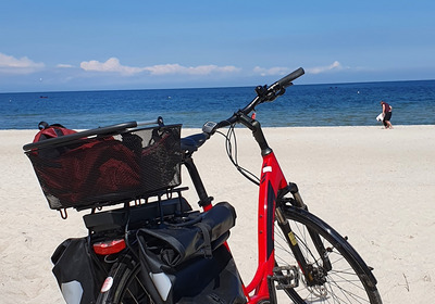 Ein Fahrrad am weißen Strand vor einem blauen Meer. Es ist ein strahlend sonniger Tag.