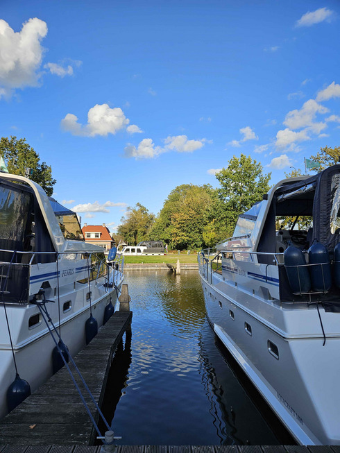 Zwei Boote liegen nebeneinander an einem Steg bei Sonnenschein.