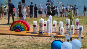 Das Bild Taufkerzen, die auf einem Tisch stehen. Im Hintergrund stehen Menschen am Fussufer