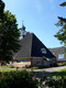 Eine moderne Kirche mit einem spitzen, schiefergedeckten Dach und einem charakteristischen Turm. An der Wand hängt eine Fahne, die die Farben der Ukraine zeigt. Umgeben von Bäumen und blühenden Pflanzen ist die Kirche in einer ruhigen, einladenden Umgebung eingebettet.