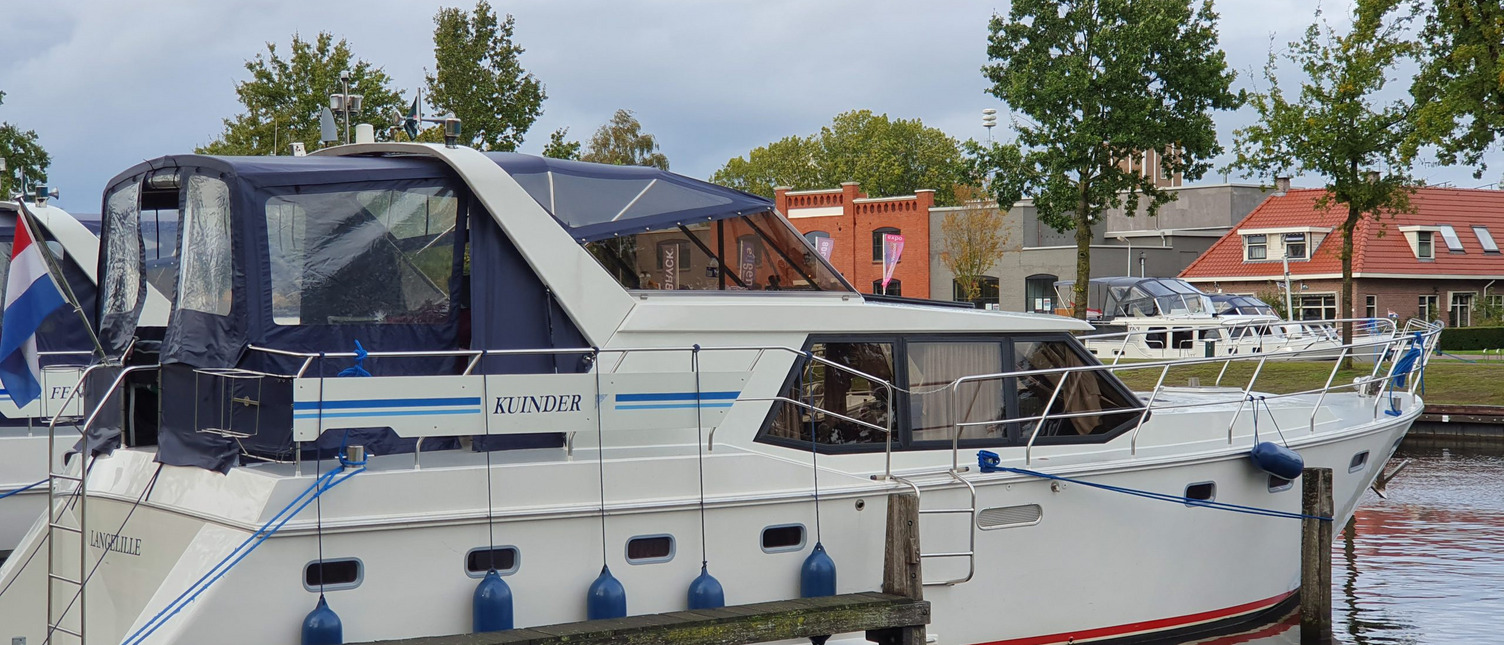 Ein Boot von der Seite fotografiert, das im Hafen festgemacht hat. Im Hintergrund sieht man weitere Boote und Häuser.
