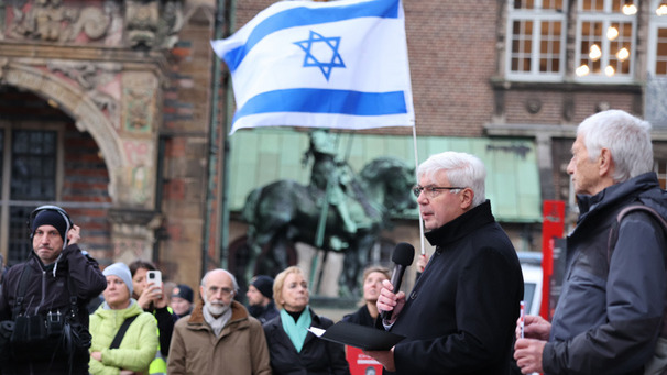Das Foto zeigt eine Solidaritäts-Demonstration für Israel auf dem Bremer Marktplatz mit Bernd Kuschnerus. Im Hintergrund eine israelische Flagge.