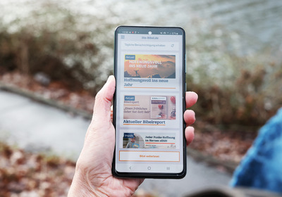 Man sieht eine Hand, die ein Smartphone hält. Auf dem Display ist eine Bibel-App zu sehen.