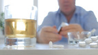 Alkohol und Tabletten stehen auf einem Tisch, dahinter sitzt eine Person.