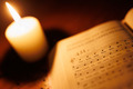 Das Foto zeigt ein aufgeschlagenes Gesangbuch und im Hintergrund eine leuchtende Kerze