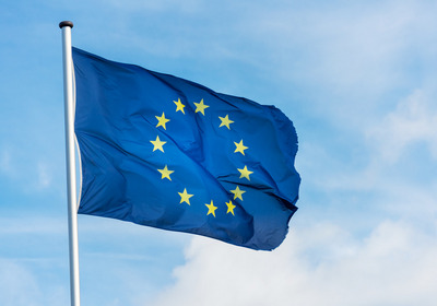Das Foto zeigt eine im Wind wehende Europaflagge (blau mit einem Kreis goldener Sterne) vor einem blauen Himmel
