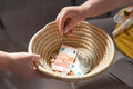 Ein geflochtenes Körbchen wird herumgereicht, um Geld einzusammeln. Ein paar Scheine und Münzen befinden sich bereits darin.