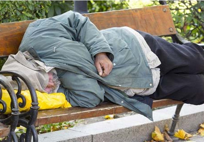 Eine obdachlose Person schläft auf einer Parkbank.