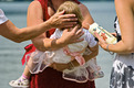 Das Foto zeigt die Taufe eines Kleinkindes und eine Patin mit einer Taukerze.