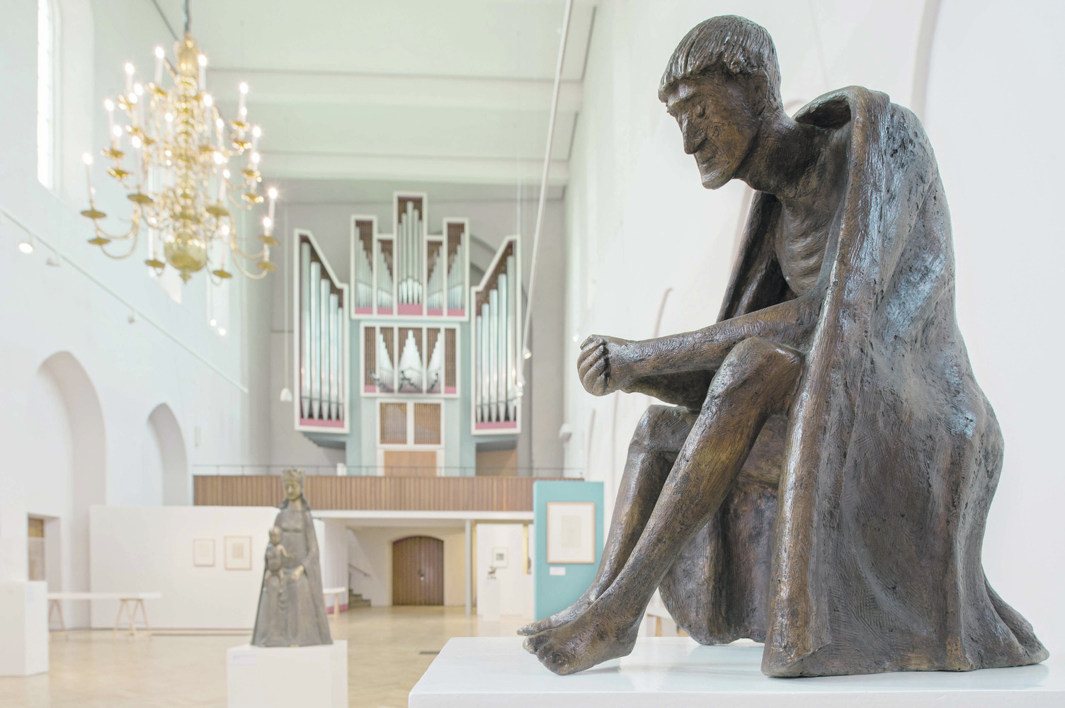 In einer Kirche ist eine Skulptur auf dem Boden sitzend zu sehenitzt  im Hintergrund d