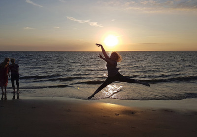 Eine Jugendliche springt am Strand vor der untergehenden Sonne