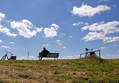 Das Bild zeigt eine Sitzbank, einen Menschen und Fahrräder