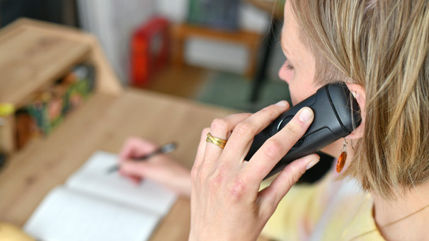 Das Foto zeigt eine Frau mit blonden Haaren an einem Schreibtisch. Sie telefoniert und ist nur leicht im Anschnitt zu sehen. Symbolbild für die Telefonseelsorge
