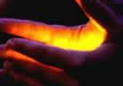 Eine Hand hält eine andere Hand, wobei zwischen ihnen ein warmes, gelb-orangefarbenes Licht strahlt. Der Hintergrund ist dunkel und verstärkt den Kontrast des Lichtes. Die Geste vermittelt ein Gefühl von Intimität und Verbindung.