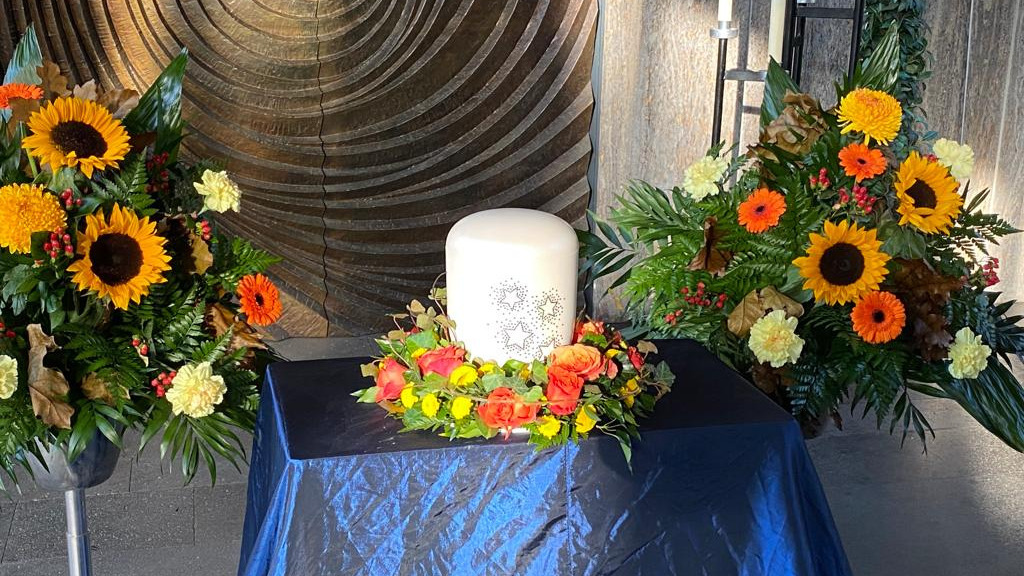 Innenansicht der Kapelle. Ein Altar mit großer Kerze. Daneben viele bunten Blumen. 