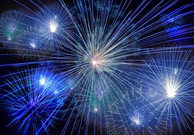 Das Bild zeigt ein spektakuläres Feuerwerk mit bunten Lichtstrahlen in Blau, Weiß und Grün, die in verschiedenen Richtungen strahlen. Der Hintergrund ist dunkel, wodurch die Lichter besonders intensiv leuchten und eine festliche Stimmung erzeugen.