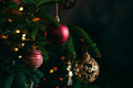 Ein Weihnachtsbaum mit grünen Nadeln, dekoriert mit roten und golden glitzernden Kugeln. Im Hintergrund scheinen warme Lichter. Die Stimmung ist festlich und gemütlich.