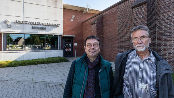 Zwei Männer stehen vor einer Gefängnismauer