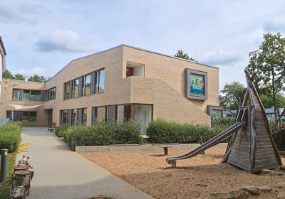 Gebäude der Kita mit Rutsche und Spielplatz im Vordergrund