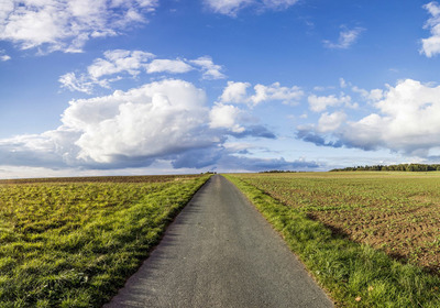 Ein kleiner Weg, daneben Felder rechts und links und der Horizont mit Wolken