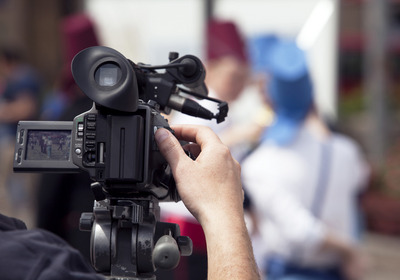 Eine Hand bedient eine Filmkamera, die eine Szene abfilmt.