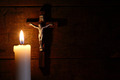 Eine Kerze erleuchtet einen dunklen Raum. An einer Wand hängt ein Kreuz mit gekreuzigtem Jesus.
