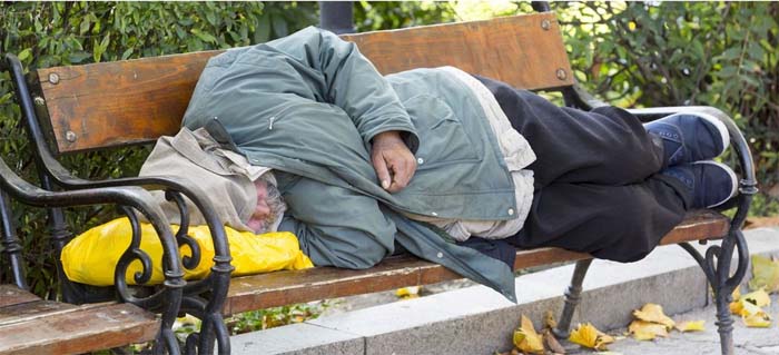 Eine obdachlose Person schläft auf einer Parkbank.