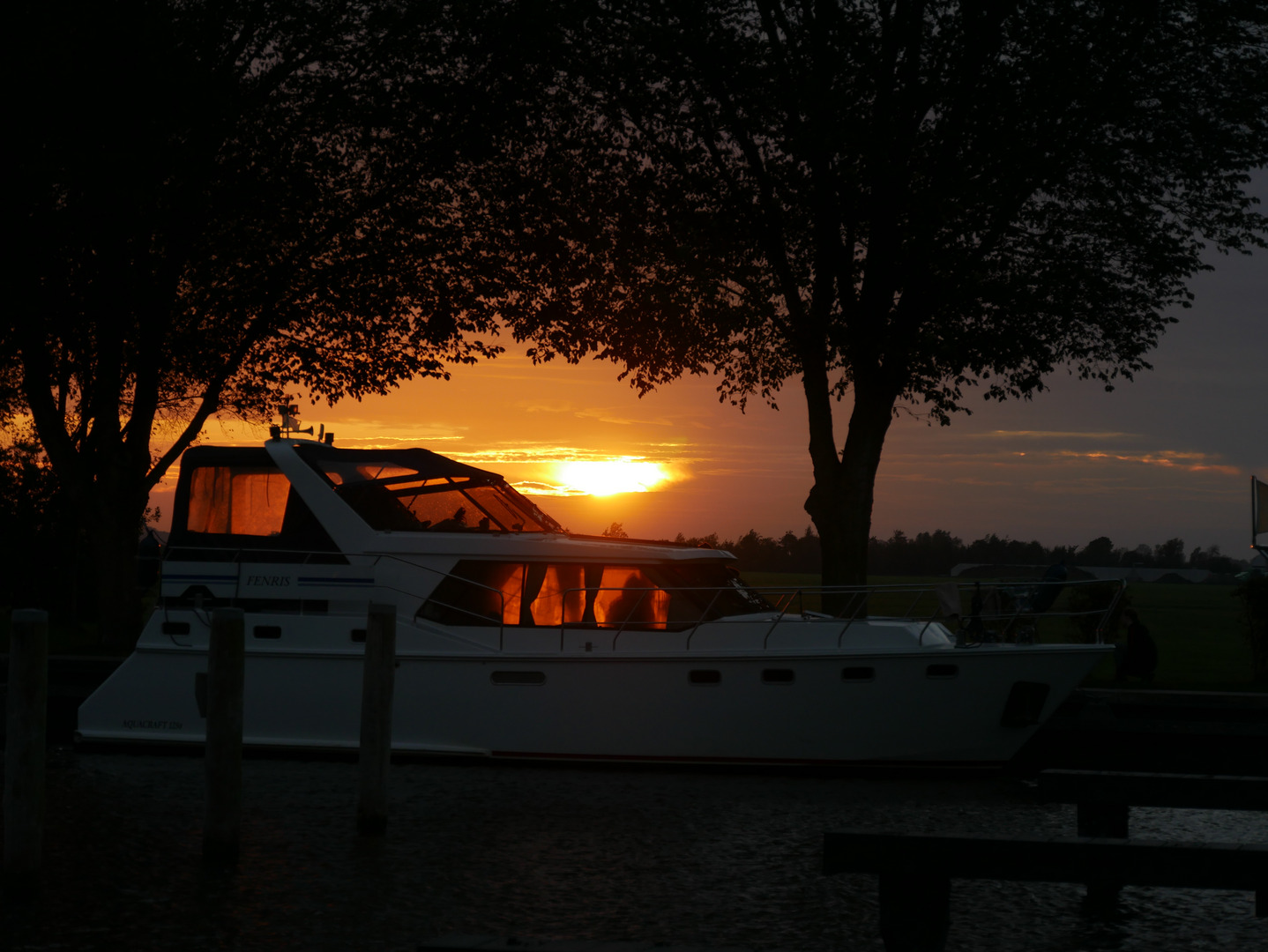 Ein Boot liegt am Steg und im Hintergrund geht die Sonne unter.