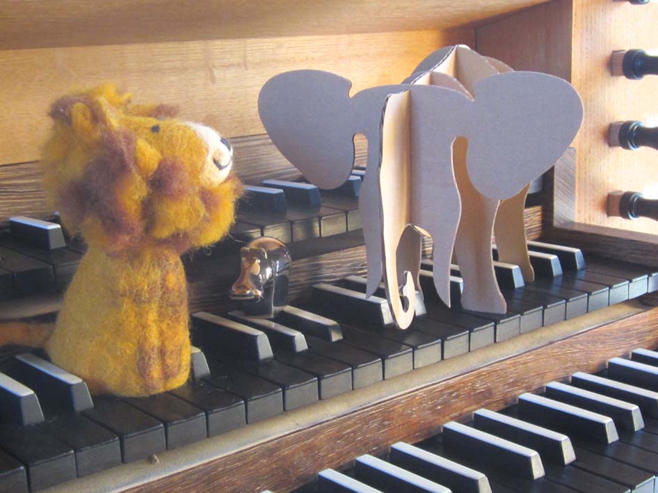 Das Foto zeigt eine Orgeltastatur, auf der ein kleiner Stofflöwe und ein Holzelefant stehen.